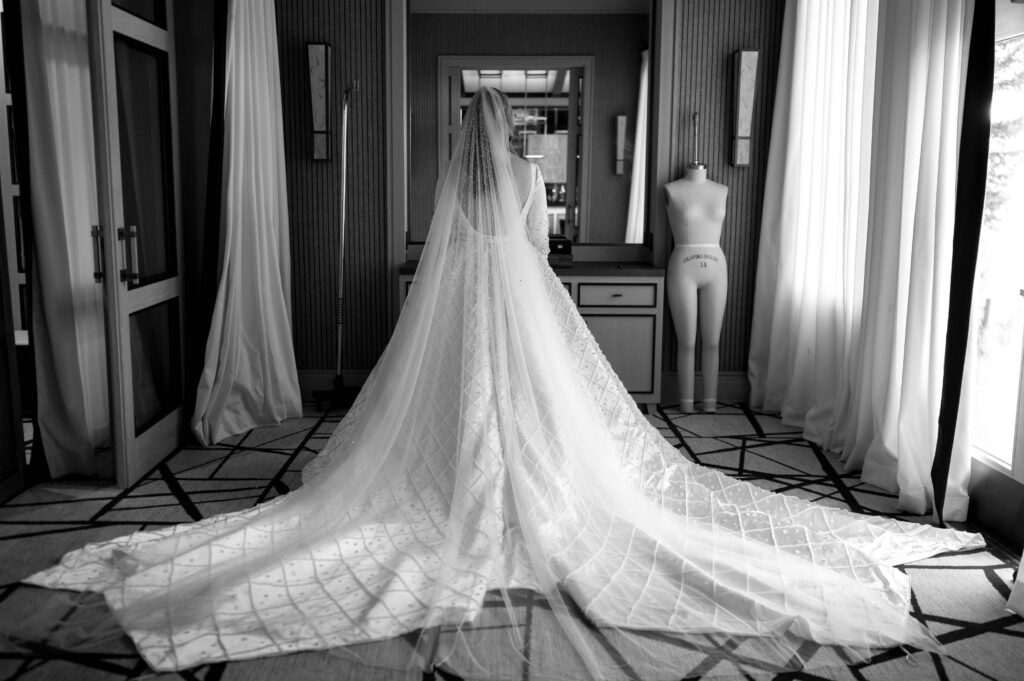 black and white photo of bride in gown and veil standing before mirror