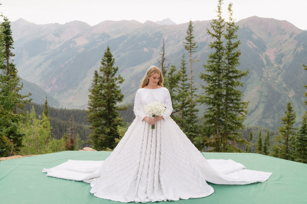 A bride wears a large wedding dress, posing in front of the Aspen mountains at The Little Nell