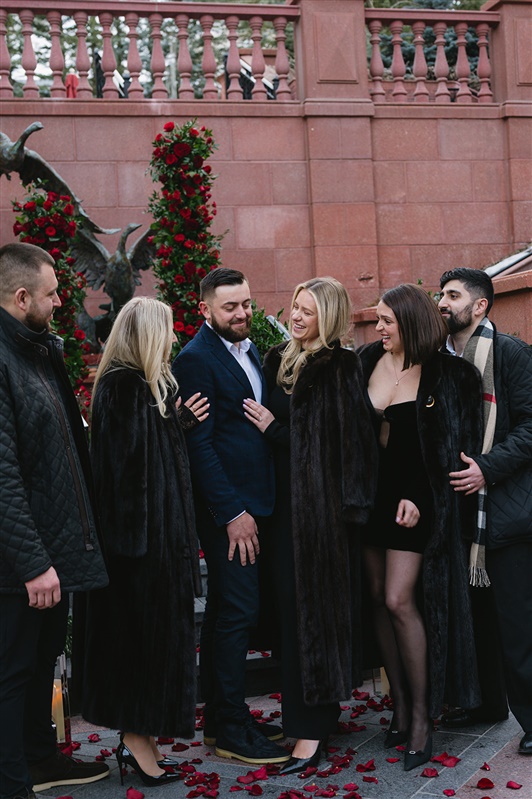 Romantic winter proposal at the St. Regis Aspen featuring a couple kissing under a dramatic red rose floral arch with snow-covered evergreens and Aspen Mountain in the background