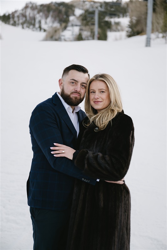 Romantic winter proposal at the St. Regis Aspen featuring a couple kissing under a dramatic red rose floral arch with snow-covered evergreens and Aspen Mountain in the background."