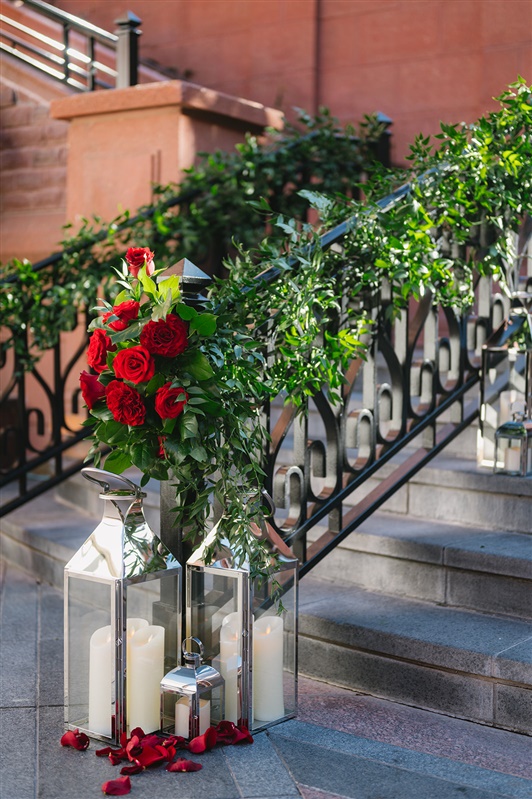 Romantic winter proposal at the St. Regis Aspen featuring a couple kissing under a dramatic red rose floral arch with snow-covered evergreens and Aspen Mountain in the background